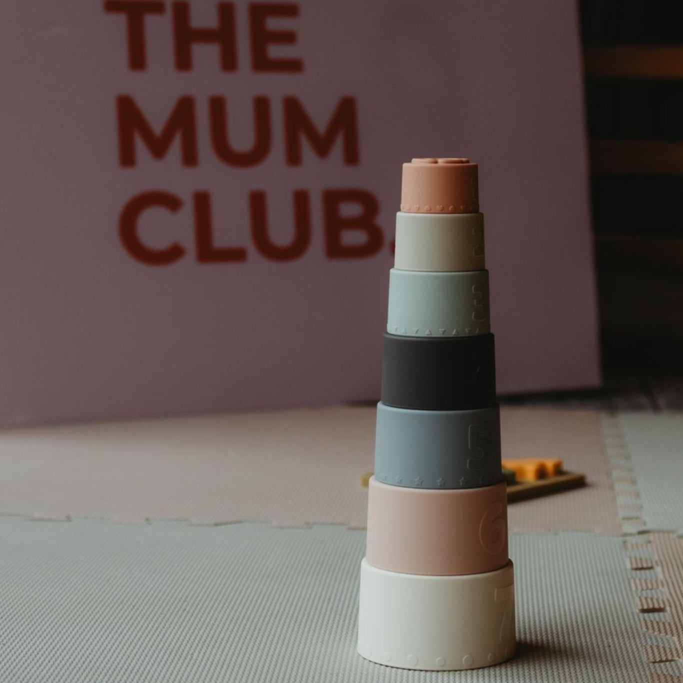 Stack of colorful cylindrical blocks on a mat with 'The Mum Club' sign in the background