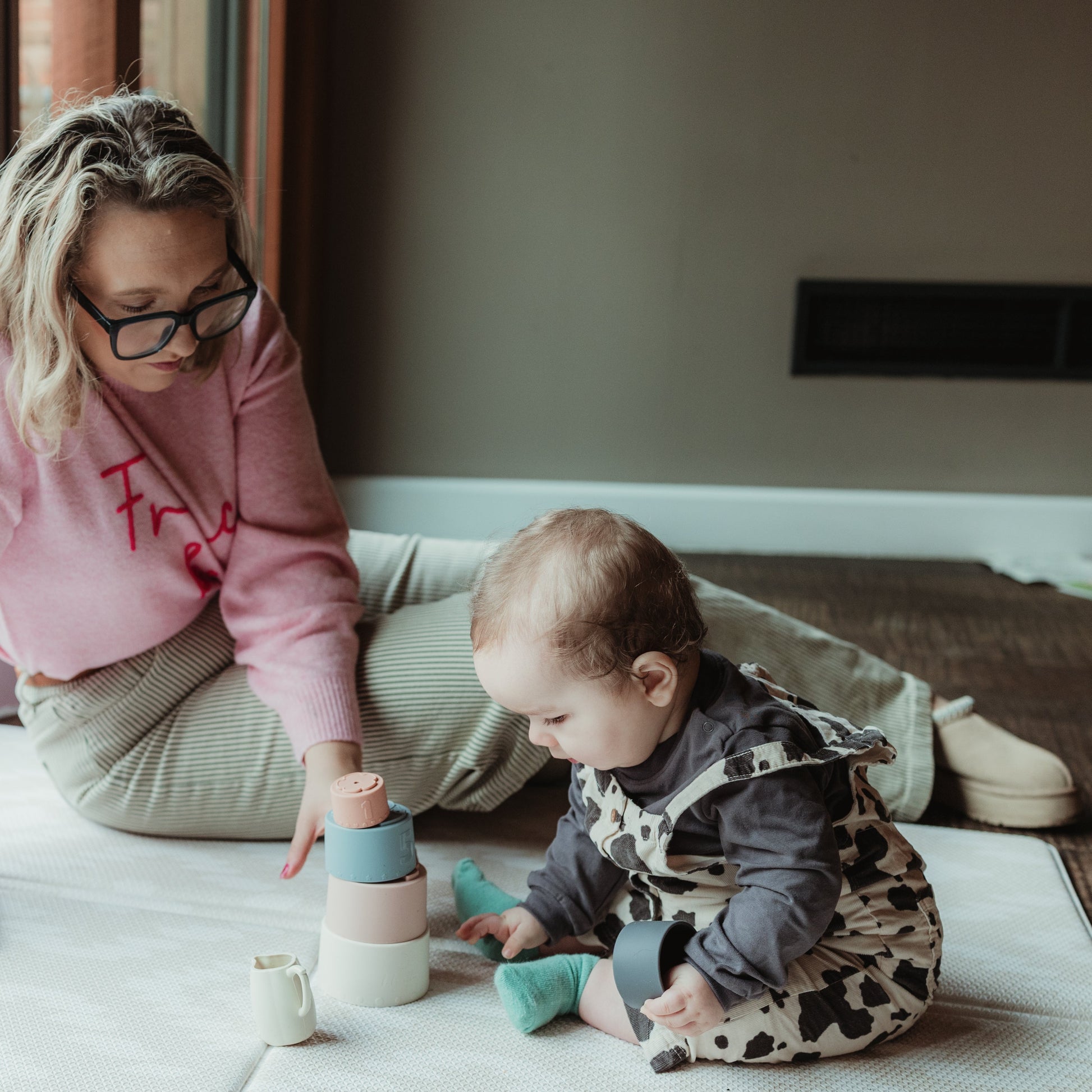 Woman and baby playing with toys on a rug in a home setting