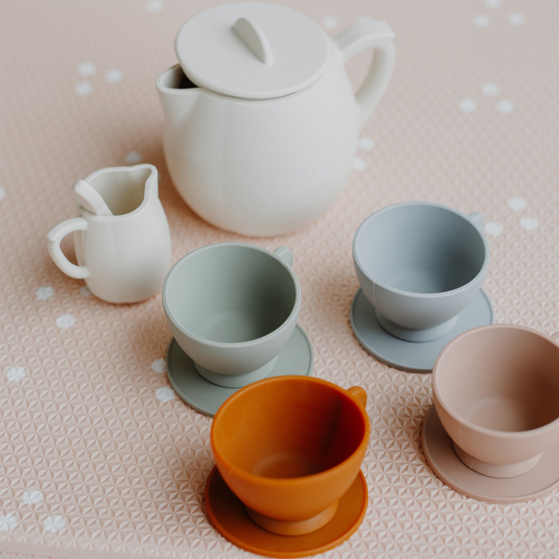 Set of silicone tea cups and teapot on a textured surface